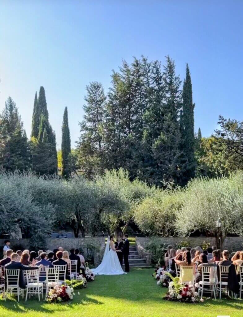 Wedding ceremony setup beneath tall trees in an Italian garden