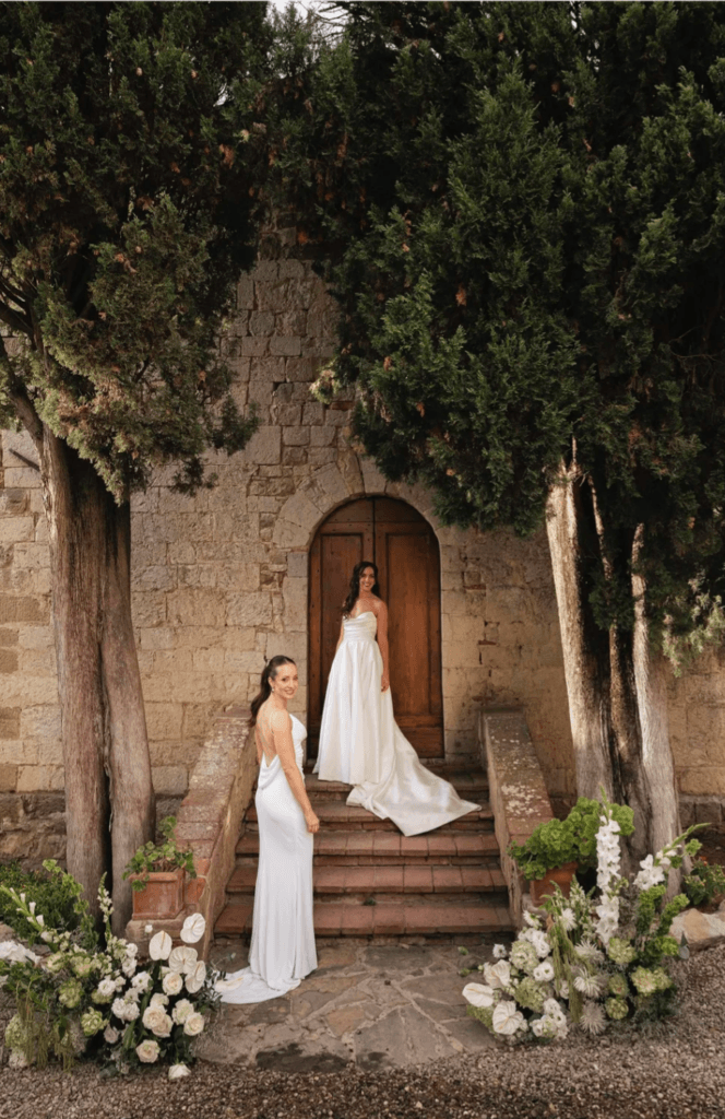 Two brides standing beneath an old stone arch at their wedding venue