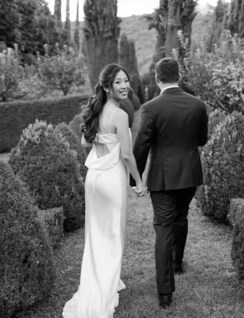 Newlywed couple walking hand in hand through an Italian garden