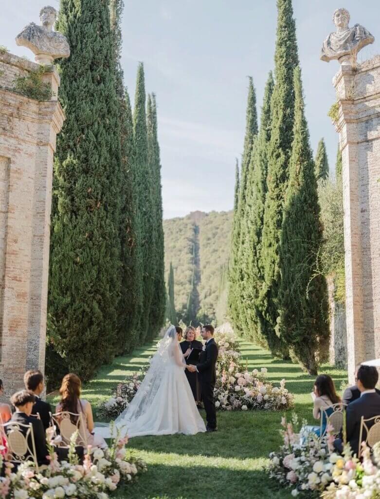 Couple and officiant during an outdoor wedding ceremony framed by cypress trees
